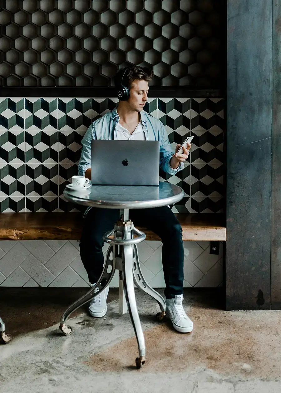 Ein junger Mann sitzt in einem Cafe und arbeitet ans seinem Laptop und hat Kopfhörer auf